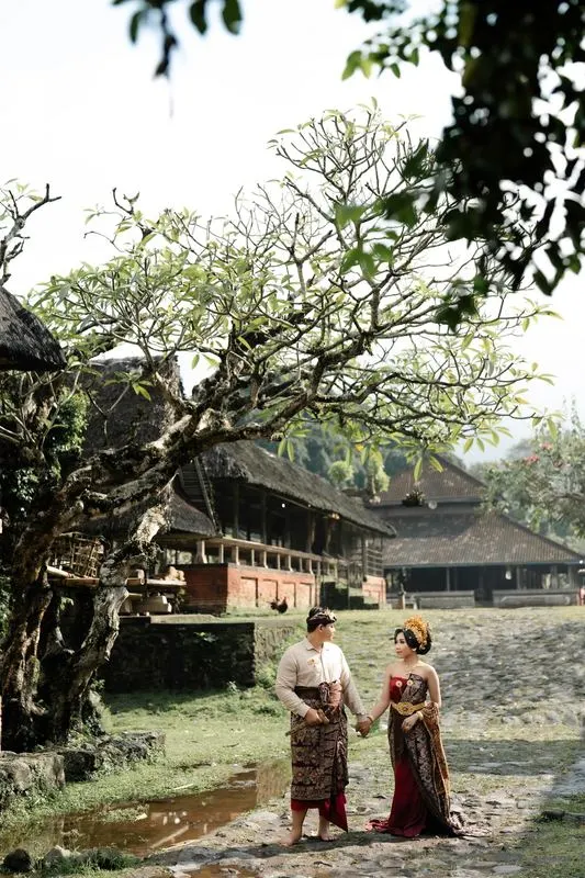Kedua mempelai bergandengan di bawah pohon kamboja